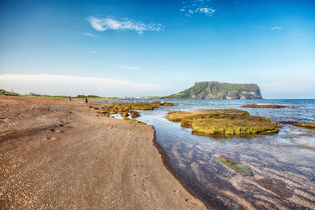 Vue panoramique de la magnifique plage de Jeju, Corée du Sud, avec ses eaux turquoise et son sable blanc. Découvrez la beauté époustouflante des plages de Jeju, avec leurs eaux cristallines et leur sable fin. Un paradis tropical à explorer lors de notre voyage en Corée du Sud avec Evans Becker. En savoir plus sur Go Corée