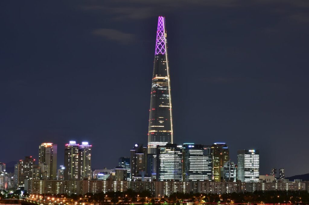 Vue nocturne de la Lotte Tower à Jamsil, Séoul, Corée du Sud, illuminée et entourée de la ville animée, Admirez la majestueuse Lotte Tower à Jamsil de nuit, illuminée et dominant le paysage urbain de Séoul. Une expérience spectaculaire lors de notre voyage en Corée du Sud avec Evans Becker. Découvrez plus sur Go Corée.