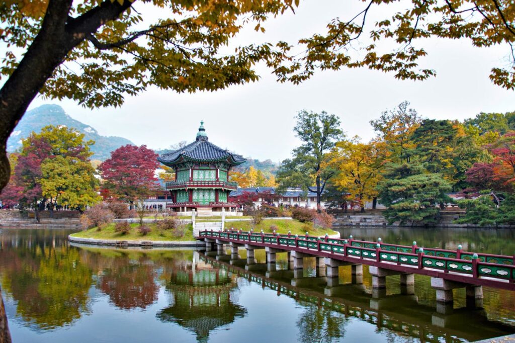 Vue du palais Gyeongbokgung en automne à Séoul, Corée du Sud, avec des arbres aux couleurs vives et un lac serein, Découvrez la beauté du palais Gyeongbokgung en automne, entouré de feuillages colorés et d'un lac tranquille. Une scène pittoresque et apaisante lors de notre voyage en Corée du Sud avec Evans Becker. Pour en savoir plus, visitez Go Corée